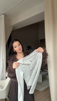 Bluză gri deschis cu mâneci lungi, cu gât larg și textură moale, având o etichetă de preț atașată. Design simplu, potrivită pentru suprapunere.