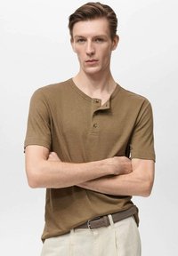 Rjava kratka majica henley z mehkega materiala, ki ima okroglo vratno izreza, gumbasti zapenjanje in teksturno podrobnost.