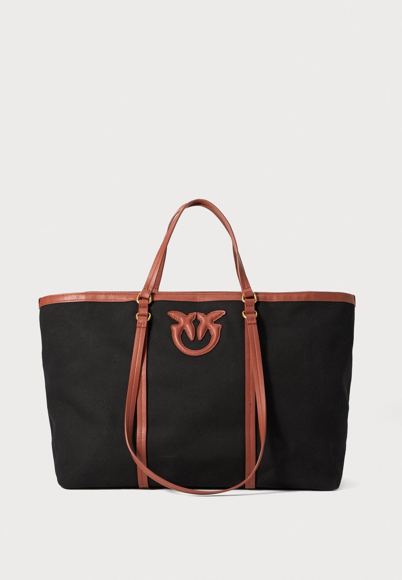 Crna platnena torba s smešnim kožnim ručkama, s reljefno logotipom sprijeda, strukturiranim oblikom i otvorenim dizajnom na vrhu.