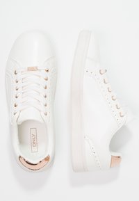 Vita sneakers i konstläder, rund tå och detaljer i roséguld. Har dekorativ sömnad och snörningsdesign.