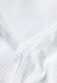 Close-up of white ribbed fabric with folded edge and visible stitching details.