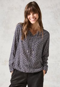 Blusa a maniche lunghe navy e bianca con motivo astratto a spirale, scollatura a V e dettagli con cordino. Indossata con pantaloni neri dal fit rilassato.