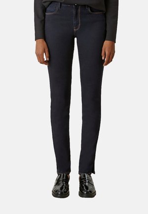Jean skinny en denim bleu foncé, avec des coutures claires et un design classique à 5 poches. Associé à des mocassins noirs brillants et un haut noir.