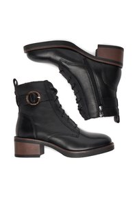 Pár černých kožených ankle bot s tkaničkami, bočním zipem, dekoračním přezkou a nízkým hnědým klínovým podpatkem na bílém pozadí.