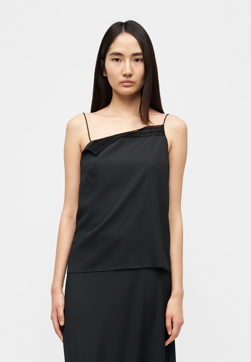 Μαύρο τοπ με λεπτές τιράντες, διακοσμημένο με δαντέλα στη μία πλευρά. Λείο, ελαφρύ ύφασμα με ασύμμετρο σχέδιο.