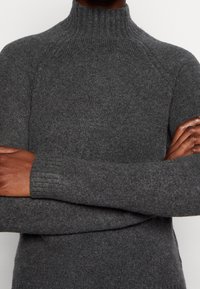 Grå höghalssweater i mjukt stickat material, med ribbade muddarna och avslappnad passform. Platta sömmar vid axlar och ärmar.