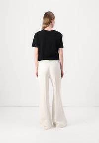 T-shirt noir à manches courtes associé à un pantalon blanc évasé. L'ensemble présente une coupe décontractée avec une texture lisse et un design simple.