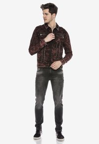 Rote und schwarze gemusterte Denimjacke mit metallischen Akzenten und Knopfverschluss, kombiniert mit grauen Slim-Fit-Jeans und dunklen Sneakern.