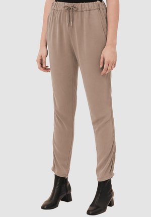 Pantalones con cintura elástica en color topo con cordón, piernas rectas, usados con botines negros de tacón en una persona de pie.