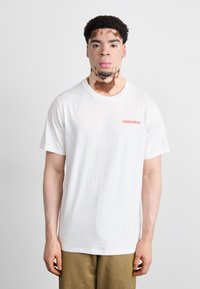 White T-shirt with round neckline and short sleeves. Features a small red "CONVERSE" logo on the left chest. Cotton fabric, relaxed fit.