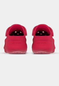 Tamancos vermelhos de borracha com calcanhares abertos e orifícios de ventilação, apresentando textura macia e a palavra "crocs" gravada no calcanhar.