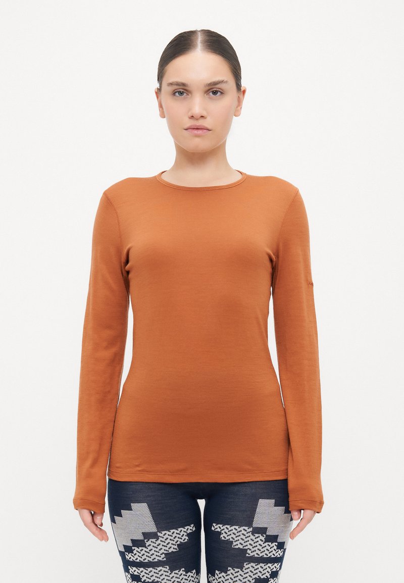 Garš sleeve, pieguļošs tops izdedžu oranžas krāsas audumā. Apaļa kakla izgriezums, gluda tekstūra, bez rakstiem. Saskaņots ar zila džinsa biksēm ar zigzag rakstu.