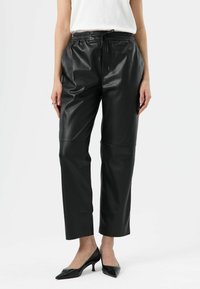 Zwarte leren broek met een ontspannen pasvorm, elastische tailleband en koorddetail; cropped lengte met een gladde, glanzende textuur.