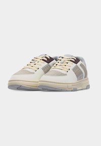 Paire de baskets basses avec des panneaux beige, gris et blancs, des lacets crème et une semelle épaisse grise sur un fond uni.