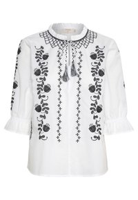 Blouse blanche avec broderie florale noire, manches trois-quarts à volants, col à volants, et un lien à l'avant avec pompons.