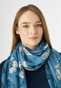 Lichtblauwe sjaal met witte bloemen- en natuurpatronen, gemaakt van zacht materiaal, gewikkeld om de nek, met een gladde textuur.