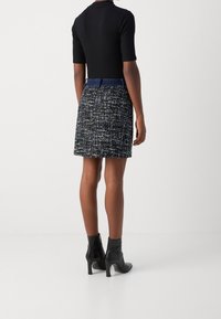 Svart tajt topp med korta ärmar, kombinerad med en mini kjol i blått och vitt tweed. Svarta stövlar med klack i ankellängd. Slät textur, strukturerad design.