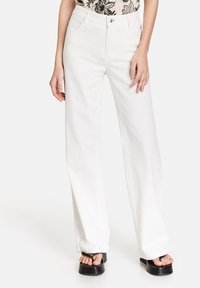 Pantalones vaqueros de pierna ancha y tiro alto, con bolsillos frontales, cierre de botón de metal y una textura suave similar al algodón.