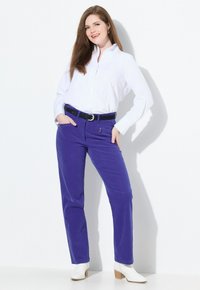 Paarse corduroy broek met zijzakken en een zwarte riem, gecombineerd met een wit overhemd en witte hakken enkellaarsjes.