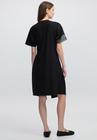 Robe noire à manches courtes, avec une finition en dentelle aux bords des manches et une coupe décontractée. Le tissu semble lisse avec une longueur au genou.