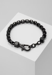 Bracelet en chaîne en métal noir avec des maillons carrés, un fermoir à homard et un accent cubique avec un détail gravé. Texture lisse, finition uniforme.