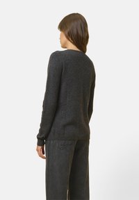 Donkere grijze trui met een zachte textuur, ronde halslijn en lange mouwen, gedragen met donkere wijde broek, gezien van achteren.