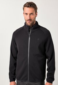 Giacca nera con zip e collo alto, in tessuto elasticizzato, con zip grigia a contrasto. Include tasche laterali e un piccolo dettaglio con logo.
