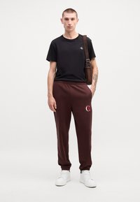 Melna T-krekls ar logo, bordo sporta bikses ar logo detaļām un baltas kedas. Šis apģērbs rada ikdienišķu, ērtu stilu.