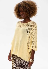 Jasnożółty sweter dzianinowy o luźnym kroju, z szerokim dekoltem i otwartym splotem. W połączeniu ze wzorzystą brązową spódnicą.