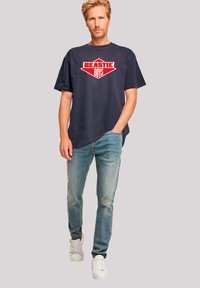 Navy graphic t-shirt with "BEASTIE BOYS" printed in red, paired with light blue distressed jeans and white sneakers. Casual fit, short sleeves.