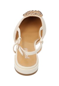 Sandalia beige con una tira para los dedos texturizada y trenzada, y un adorno metálico con joyas en la parte delantera, con una correa en el tobillo y una suela plana.