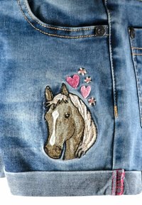 Denimtyg med broderad hästhuvud, rosa hjärtan och små blommor nära en knapp och fick söm.