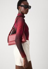 Red leather handbag with a structured rectangular design and adjustable strap, paired with a maroon gradient long-sleeve top and white shorts.
