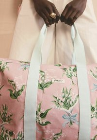 Torba typu duffel w różowy kwiatowy wzór z zielonymi liśćmi i białymi liliami. Światło-niebieskie uchwyty z tkaniny i etykieta z boku.