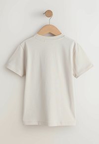 Tricou scurt bej deschis, din bumbac, cu decolteu rotund și fără imprimeuri sau modele vizibile, afișat pe un umeraș din lemn.