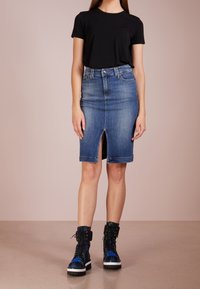 Žena v černém krátkém rukávu, modré džínové sukni do kolen s předním rozparkem a černých šněrovacích botách s modro-zeleným kostkovaným vzorem.