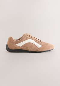 Baskets en daim beige avec un accent blanc incurvé, lacets à l'avant, bout arrondi et semelle en caoutchouc noire, présentant des détails de surface texturée.