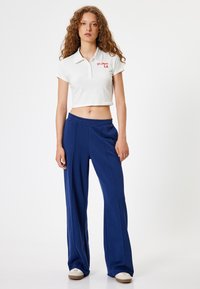 Camisa polo blanca corta con el texto rojo "Los Ángeles", combinada con pantalones de pierna ancha en color marino que cuentan con una cintura elástica y detalles de pliegues.