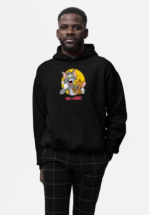 Sort hættetrøje med et grafisk billede af Tom og Jerry mod en gul baggrund, med teksten "TOM og JERRY" i rød.