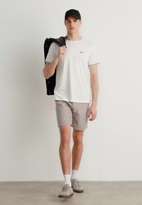 White crew neck t-shirt with black and white trim, gray shorts, carrying a black jacket, and wearing gray shoes and a black cap.