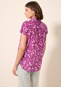 Korte mouwen, roze blouse met een textuur, abstract patroon, een lichte high-low zoom en geplooide achterkant voor extra volume.