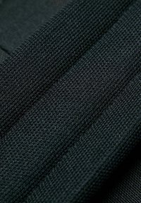 Tessuto nero testurizzato con un design a coste, caratterizzato da variazioni nella tessitura e una colorazione scura uniforme in tutto l'elemento.