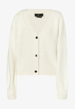 Balts, īss kardigans no pūkainas auduma. Tam ir dziļš V veida kakls, ribotas piedurknes un trīs melnas pogas priekšpusē.