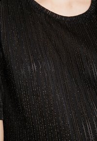 Svart kortärmad topp med en texturerad mönstring av vertikala ränder och subtil metallisk glans. Rundad halsringning, slät tygfinish.