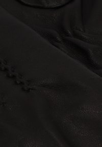 Zwart lederen stof met een gestructureerd oppervlak en subtiele glans, met contrasterende stikseldetails langs één rand.