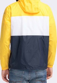 Chaqueta resistente al agua con una sección superior amarilla, una franja blanca en el medio y una sección inferior azul marino. Incluye capucha y puños elásticos.