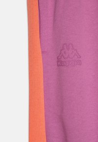 Lila och orangea träningsbyxor med en mjuk textur, med en Kappa-logotyp präglad på den lila delen.