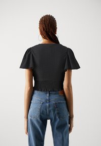 Černý texturovaný crop top s nadýchanými krátkými rukávy, spárovaný s vysoce pasovými světle modrými džíny s klasikým pěti-kapsovým designem a logem.