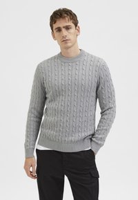 Suéter de punto trenzado en gris claro con cuello redondo y puños y dobladillo acanalados. La tela tiene un aspecto texturizado.
