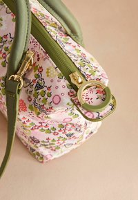 Borsa a mano con stampa floreale multicolore, accessori in oro, rifiniture verde e forma strutturata. Presenta una chiusura con zip e una tracolla staccabile.